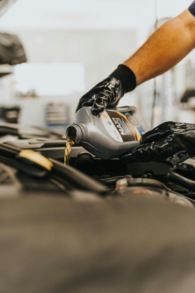 pexels-photo-13065693-13065693 Close-up of a mechanic pouring engine oil into a car engine with gloved hands, indoors.